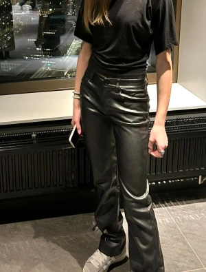 Bikbok  Svarta raka skinnbyxor Stl 34 skinn byxa  - Snygga svarta skinnbyxor från Bikbok med rak passform och normal midja. Byxorna har klassiska fickor fram och bak, bälteshällor och stängs med knapp och dragkedja. Perfekta för dig som vill ha en cool och stilren look.