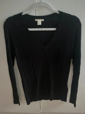Svart ribbad v-ringad tröja - Svart långärmad tröja från H&M med ribbad struktur och snygg v-ringning. Perfekt för dig som gillar stilrena och enkla plagg med lite edge. Passar dig som vill ha en klassisk look