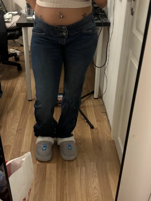 Blå bootcut jeans från Bershka - Säljer ett par mörkblå jeans från Bershka med bootcut passform och låg midja. Jeansen har klassiska fickor både fram och bak samt stängs med dubbla knappar och dragkedja. Materialet är bomull med lite stretch för extra komfort.