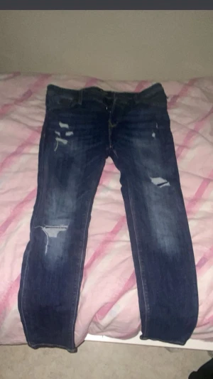 Blå slitna jeans från Jack & Jones - Snygga blå jeans från Jack & Jones med slitningar och  detaljer på benen för en cool look. Klassisk femficksmodell med normal passform och rak siluett. Jeansen har medelblå tvätt och är tillverkade i mjukt bomullsmaterial. Helt ny! Storlek w33l32