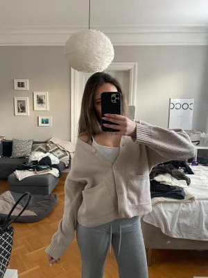 Beige oversized kofta med knappar - Supermjuk och oversized beige kofta med stora fickor framtill och knappar. Koftan har en avslappnad passform, v-ringning och långa ärmar. Perfekt att slänga över ett linne för en chill look.