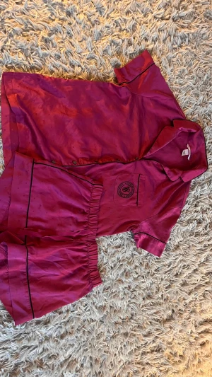 Mörkrosa satin set från Victoria's Secret XS - Snyggt  mörkrosa satin set från Victoria's Secret Signature med svarta detaljer och diskret prickmönster. Shortsen har elastisk midja och en mjuk, glansig finish som känns lyxig. Perfekt för chill hemma eller som pyjamas. Matchande skjorta i samma material i nyskick. Kvitto finns köpt i nyc 2024