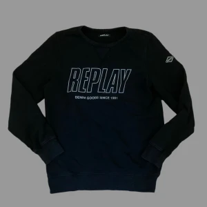 Svart sweatshirt från Replay - Svart sweatshirt från Replay med stort tryck på bröstet och rund hals. Tröjan har långa ärmar och en liten logga på vänster ärm. Mjuk bomullskvalitet och klassisk passform, perfekt för chill dagar.