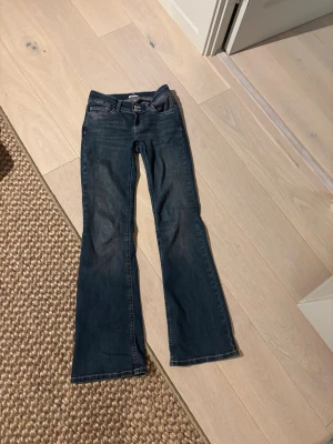 Blå bootcut jeans från Nelly - Snygga blå jeans från Nelly med bootcut passform och klassisk femficksdesign. Jeansen har vita dekorativa sömmar på bakfickan och dubbla silverfärgade knappar i midjan. Perfekt för dig som gillar en retro vibe och vill ha lite extra sväng i benen. 