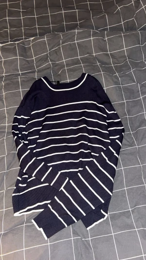 Mörkblå randig stickad tröja - Snygg mörkblå stickad tröja med vita horisontella ränder och rund hals. Tröjan har långa ärmar och ribbade muddar vid ärmslut och nederkant. Perfekt för dig som gillar klassisk och chill stil.