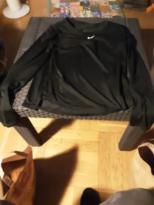 Svart långärmad Nike tröja - Svart långärmad tröja från Nike med klassisk vit logga på bröstet. Tröjan har en enkel och clean design, perfekt för träning eller chill. Materialet känns lätt och smidigt mot huden. Passar dig som gillar sportiga och stilrena plagg.