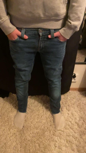 Mörk/ljus blåa nudie jeans - Säljer nu mera ett par nudie jeans. Personen på bilden är 165-170. Skriv vid funderingar. OBS av klippta nere vid benen men inget man märker.
