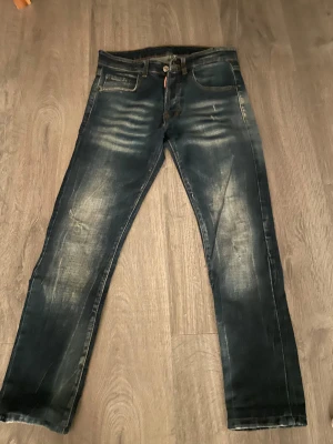 Mörkblå jeans från Dsquared2 - Snygga mörkblå jeans från Dsquared2 med slitna detaljer och kontrastsömmar. Klassisk femficksmodell med röd Dsquared2-tag vid fickan. Jeansen har en rak passform och är tillverkade i robust denim för en cool look.