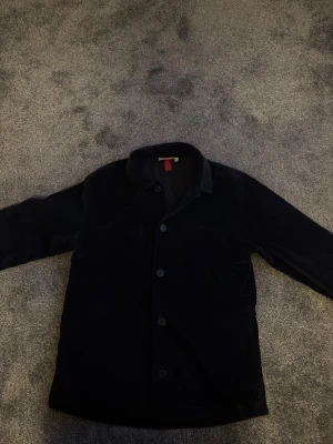 Marin blå manchesterjacka från s.Oliver L - Stilren marin blå manchesterjacka från s.Oliver i storlek L. Klassisk overshirt-modell med knäppning framtill och två bröstfickor. Mjuk manchester ger en cool och avslappnad vibe. Perfekt för lager-på-lager och funkar året runt.