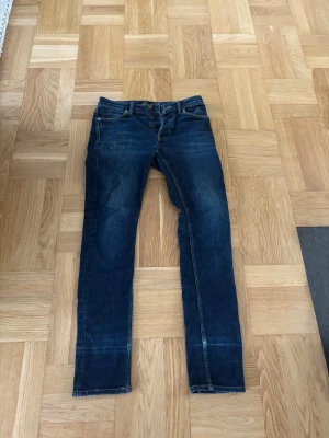 Mörkblå slim jeans från Neuw, 28/32 - Snygga mörkblå jeans från Neuw i modellen Lou Slim. Klassisk femficksdesign, smal passform och kontrastsömmar. Jeansen är tillverkade i stretchigt bomullsmaterial och har en stilren look med subtila slitningar. Perfekta för dig som gillar en modern och clean stil. Säljer byxorna då dom är för små för mig