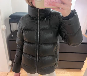 Colmar Jacka - Svart, glansig pufferjacka från Colmar med hög krage och dragkedja framtill. Colmar-logga på ärmen och quiltad design som ger en cool vibe. Sparsamt använd och i mycket fint skick. Köpt för ca 6.500kr.❤️Kom med bud!  