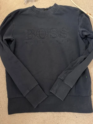 Mörkblå sweatshirt från Hugo Boss - Snygg mörkblå sweatshirt från Hugo Boss med broderad logga på bröstet. Tröjan har rund hals, långa ärmar och breda ribbade muddar vid ärmslut och nederkant. Perfekt för dig som gillar stilrena och klassiska plagg med premiumkänsla.
