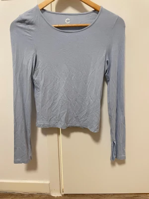 Ljusblå långärmad topp från Cubus - Säljer en ljusblå långärmad topp från C med rund halsringning och slitsdetalj vid ärmsluten. Toppen har en clean och enkel design, perfekt för att styla med dina favoritjeans eller kjol. Materialet är mjukt och stretchigt för en skön passform.