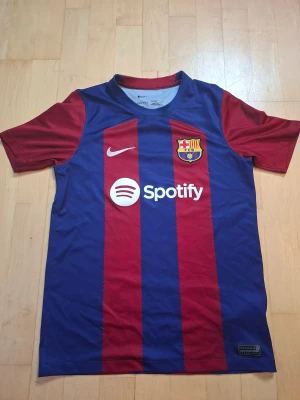 FC Barcelona Nike fotbollströja L - Snygg FC Barcelona matchtröja från Nike med klassiska blå och röda ränder, klubbmärke på bröstet och Spotify-logga. Tillverkad i Dri-Fit material som andas. Kortärmad modell med rund hals och autentisk badge nertill.