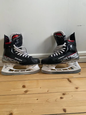 Bauer Vapor 3X hockeyskridskor svart - Säljer ett par Bauer Vapor 3X hockeyskridskor i svart med vita och röda detaljer. Skridskorna har snörning med vita skriskosnören, dock har toppen av snöret på ena skridskon blivit avtrampad men dem funkar endå. Man kan byta snörerna om man vill. Det är vaxade snören och skridskon en robust konstruktion i syntetmaterial. Sulan är vit och tåpartiet är rundat för extra komfort på isen. Storlek 5,5 fit 1