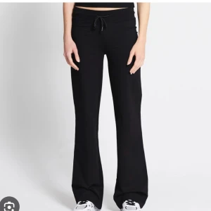 Svarta bootcut mjukisbyxor med snörning - Svarta mjukisbyxor med bootcut-ben och snörning i midjan. Byxorna har en avslappnad passform och är perfekta för en chill och sportig stil. Tillverkade i mjukt material som känns skönt mot huden.