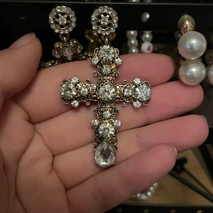 Korsörhängen med stenar - Säljer ett par stora statement-örhängen i form av kors, dekorerade med gnistrande klara stenar och guldfärgad metall. Örhängena har en lyxig vibe med många detaljer och stora droppformade stenar längst ner. Perfekta för dig som vill sticka ut och älskar bling! Köpa från Urban Outfitters😇Aldrig använda!