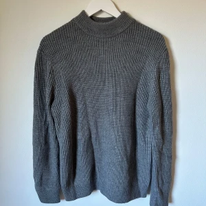 Grå stickad tröja från H&M - Mysig grå stickad tröja från H&M med högre ribbad krage och långärmad modell. Tröjan är i grovstickat material och passar perfekt när det är kyligt ute. Tillverkad i 95% akryl och 5% ull för en skön känsla. 3R21