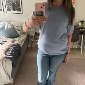 Ljusblå t-shirt från Å Woman, M - Enkel och stilren ljusblå t-shirt från Å Woman i storlek M. T-shirten har rund halsringning, korta ärmar och är gjord i mjuk bomull. Perfekt för en chill och avslappnad look. Den har en fläck på magen som jag inte riktigt vet om den går bort