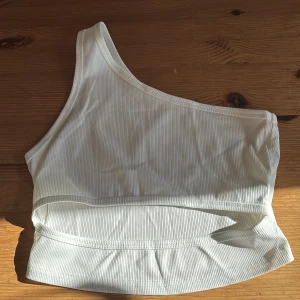 Vit ribbad one shoulder topp - Säljer en vit ribbad topp med one shoulder-design. Toppen är croppad och har en tight passform som framhäver axlarna. Perfekt för dig som gillar minimalistisk stil och vill ha något enkelt men ändå trendigt.