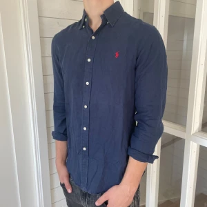 Ralph lauren linneskjorta - Säljer denna riktigt snygga mörkblåa linneskjortan från Ralph lauren! Den är i mycket bra skick och har inga defekter, storlek M modell slim fit, den är 80 cm lång och 50 cm bred under armhålorna, jag på bilderna är 184 cm och väger 80 kg, hör gärna av dig vid frågor!