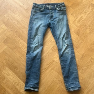 Blå slim fit från Neuw - Snygga blå jeans från Neuw med skinny passform och klassisk femficksdesign. Jeansen har slitningar och en liten reva på ena benet för en cool, avslappnad look. Tillverkade i mjukt denim med dragkedja och knapp i midjan. De är waist 32 och längd 32. Kostar ca 1300 nya