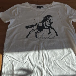 Vit t-shirt med hästtryck från XOXO friends - Vit t-shirt köpt från Ullared med svart tryck av en galopperande häst och texten 'Stardust' framtill.