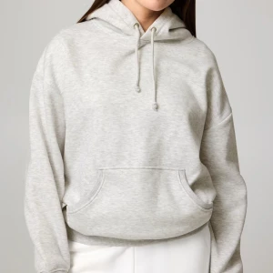 Ljusgrå hoodie med huva och ficka - Säljer en ljusgrå hoodie med klassisk huva och snörning. Tröjan har en stor magficka och är tillverkad i mjukt material, perfekt för chill dagar. Passformen är loose och ärmarna är långa för extra komfort.