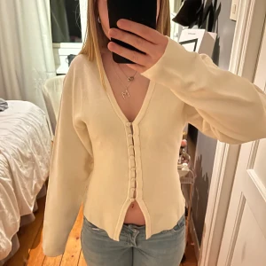 Krämvit kofta med knappar från Gina Tricot - Superfin krämvit kofta från Gina Tricot med v-ringning och klädda knappar framtill. Långärmad modell. Den har prislappen kvar och är aldrig använd. Slutsåld online 💓