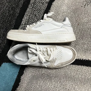 Vita sneakers från Gant i skinn och mocka - Snygga vita sneakers från Gant med detaljer i ljusgrå mocka och klassisk snörning. Skorna har rund tå, perforeringar på tån för extra ventilation och Gant-logga på sidan. Yttermaterialet är en mix av skinn och mocka, vilket ger en stilren och fräsch look. Passar bra på killar och tjejer.