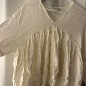 Vit volangblus från Second Female - Luftig och romantisk vit blus från Second Female med v-ringning och volangdetaljer. Blusen har trekvartsärmar med resår och är tillverkad i ett tunt, lätt material som ger en flowy känsla. Perfekt för dig som gillar en avslappnad men ändå chic stil.