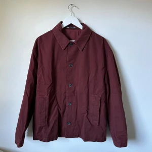 Vinröd skjortjacka från Zara i bomull - Vinröd overshirt från Zara i 100% bomull. Jackan har klassisk krage, raka ärmar, knäppning framtill med svarta knappar och två stora fickor. Enkel och stilren modell som passar perfekt till lager-på-lager under höst och vår. 3T15