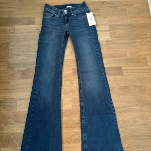 Bootcut jeans i mörkblå denim från Nelly - Mörkblå bootcut jeans från Nelly med låg midja och snygga kontrastsömmar. Klassisk femficksmodell med dubbla knappar framtill och dekorativa sömmar på bakfickorna. Aldrig använda och prislappen sitter på🫶🏻