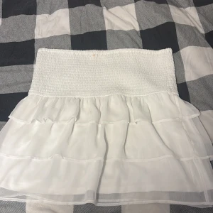 Vit volangkjol från BikBok XS - Supersöt vit kortkjol från BikBok i storlek XS. Kjolen har bred smock i midjan och flera lager med volanger som ger en luftig och flowy känsla. Perfekt för en fräsch och somrig look! Passar även att ha strumpbyxor till under till höst om man skulle vilja.