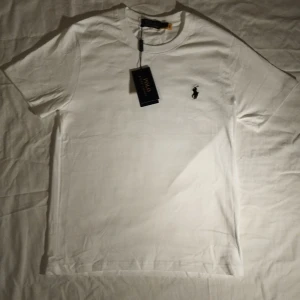 Vit t-shirt från Polo Ralph Lauren - Vit t-shirt från Polo Ralph Lauren med klassisk svart broderad logga på bröstet. T-shirten har rund hals, korta ärmar och är gjord i mjuk bomull. Enkel och stilren design som passar till allt.