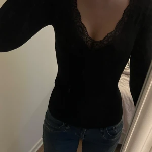 Svart långärmad spetsblus - Säljer en svart långärmad blus med v-ringning och fina spetsdetaljer längs urringningen. Toppen har en slim passform och är perfekt för dig som gillar en stilren men ändå feminin look.