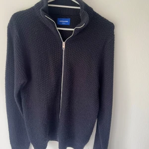 Full-zip från Jack &Jones - Säljer en mörkgrå stickad tröja från Jack & Jones. (Helt ny!)Tröjan har hög krage och lång ärm. Perfekt för kyligare dagar och enkel att matcha med olika outfits. Kontakta mig vid minsta fundering 