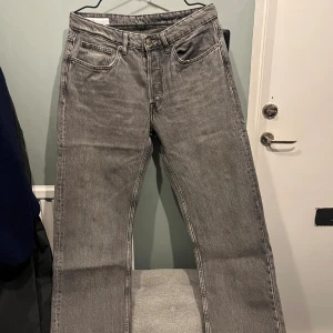 Grå raka jeans från Zara, stl 42 - Grå jeans från Zara i rak modell med klassisk femficksdesign och knappgylf. Jeansen har en stilren look och är tillverkade i bomull. Perfekta för dig som gillar en enkel och clean stil. Storlek 42 (32/32).