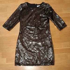 Glittrig svart paljettklänning - Supersnygg svart kortklänning täckt av glittrande paljetter. Klänningen har trekvartsärm och en smickrande, figurnära passform. Dragkedja baktill för enkel påklädning. Perfekt för dig som vill sticka ut och glänsa. (Pris kan diskuteras)