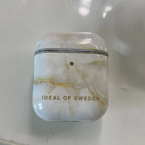 Ideal of Sweden AirPods Case Marble - Snyggt marmormönstrat skyddsfodral från Ideal of Sweden för AirPods. Fodralet har guldfärgade detaljer och är i gott skick med mindre slitage runt kanterna. Perfekt för att ge dina AirPods ett exklusivt utseende och extra skydd.