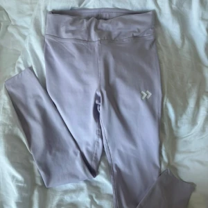 Ljuslila träningsbyxor från Lager 157 - Snygga ljuslila leggings från Lager 157 med hög midja och snörning i linningen. Materialet är stretchigt och perfekt för träning. Diskret logga på benet och praktisk ficka i midjan. Supersköna och stilrena för gymmet eller löprundan