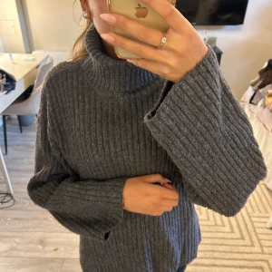 Grå ribbad polotröja med vida ärmar - Mysig grå polotröja med bred ribbstickning och vida ärmar. Tröjan har hög krage och en loose fit som ger en chill vibe. Perfekt för lager-på-lager och passar till både jeans och kjol.