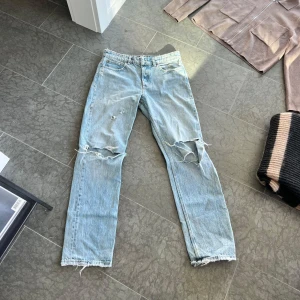 Ljusblå slitna  jeans Zara - Ljusblå zara jeans med raka ben och klassisk femficksdesign. Jeansen har slitna detaljer och revor vid knäna för en cool, avslappnad look. Tillverkade i 100% bomull med råa kanter nertill för extra edge.