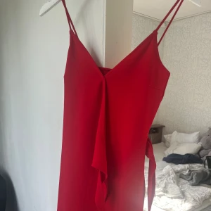 Röd omlottklänning från H&M Divided - Snygg röd kortklänning från H&M Divided med tunna axelband och omlottdetalj framtill. Klänningen har knyt i sidan och en enkel, stilren design som ger en trendig look. Perfekt för dig som gillar färg och vill sticka ut.
