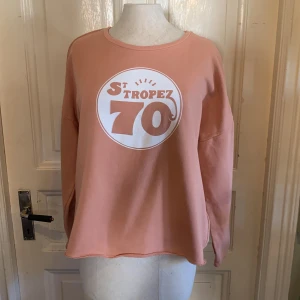 Rosa St Tropez 70 sweatshirt - Säljer en oversized sweatshirt i ljusrosa med tryck 'St Tropez 70' framtill. Tröjan har rund halsringning, långa ärmar och en loose passform. Perfekt för en chill och avslappnad stil.