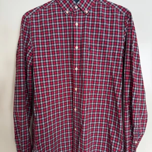 Peak Performance skjorta  - Rutig skjorta i rött, blått och vitt från märket Peak Performance. Klassisk button-down krage, långärmad och med bröstficka. Skjortan har vita knappar och är tillverkad i mjuk bomull, perfekt för en avslappnad och snygg look.
