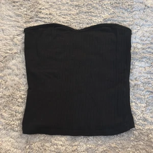 Svart ribbad tubtopp - Svart ribbad tubtopp från SHEIN i storlek XS, passar även S. Toppen är bandeau-modell och har en enkel, stilren look med diskreta vertikala ränder. 