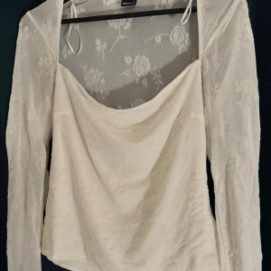 Vit meshblus med blommönster Gina Tricot - Superfin vit meshblus från Gina Tricot i storlek L. Blusen har långa ärmar, transparent mesh med broderade blommor och en snygg draperad urringning. Perfekt för dig som gillar romantiska och trendiga detaljer.