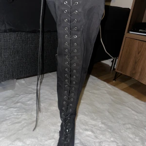 Svarta stövletter med snörning Truffle - Säljer ett par svarta stövletter från Truffle Collection med spetsig tå och hög klack. Skorna har snörning framtill, dragkedja på insidan och är gjorda i ett syntetmaterial med matt finish. Perfekta för dig som vill sticka ut med en edgy look.