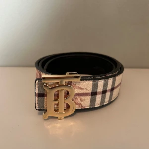 Burberry bälte med rutigt mönster - Snyggt Burberry bälte med klassiskt rutigt mönster i beige, svart och vinrött. Lite slitet som man ser på bild 2 men annars bra skick! Tveka inte att höra av dig!☺️